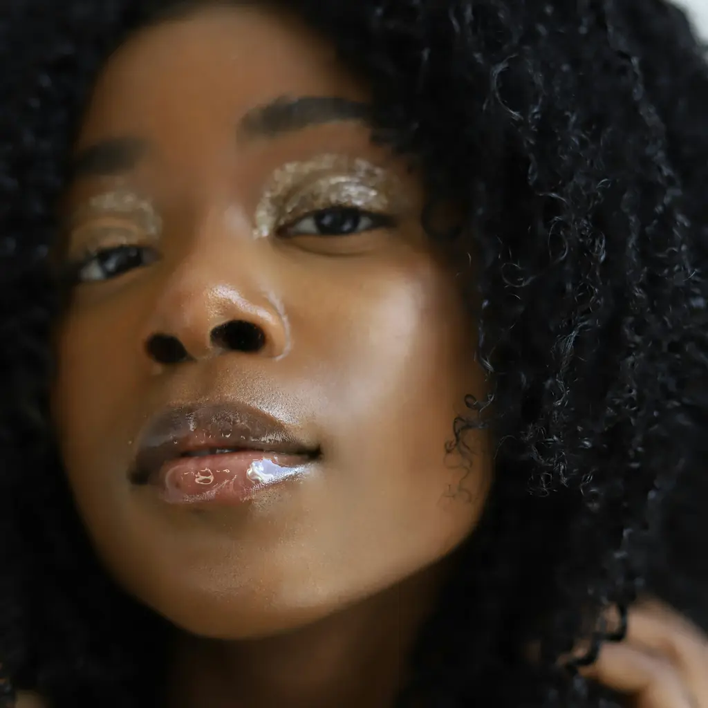 Rosto de uma mulher negra de cabelo cacheado, com a pele natural e iluminada.